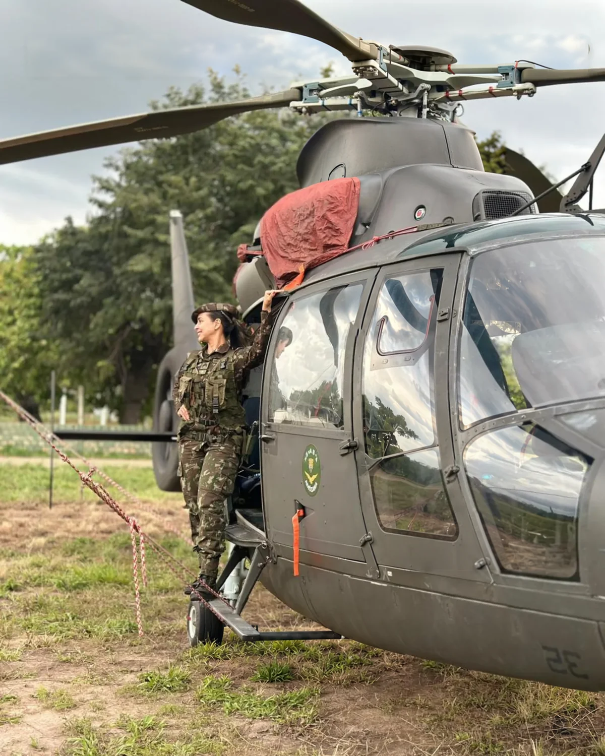 Suellen como enfermeira militar do Exército, ao lado de um helicóptero